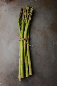 A single bunch of Asparagus tied with twine on a metal cooking sheet. Vertical format shot from a high angle. 