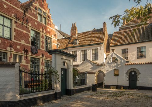 Kortrijk, Flanders, Belgium - September 17, 2018: Twilight falls on corner of the beguinage with white and red brick housing. Gray courtyard. Some green foliage.