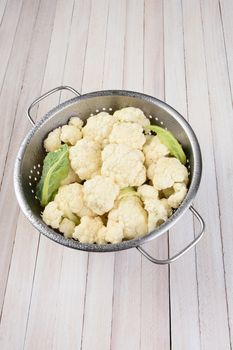 Vertical high angle view of a head of cauliflower in a metal colander on a rustic wood table, with copy space.