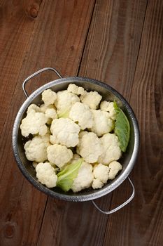 High angle view of a colander filled with cauliflower florets. On a rustic wood table. Vertical format.