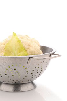 Closeup of a head of Garden Fresh Cauliflower in Colander on a white surface misted with water drops. Vertical format.