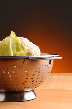 Fresh picked cauliflower in a metal colander on rustic wooden table. Vertical format with a black background.