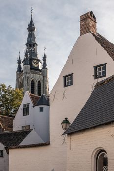 Kortrijk, Flanders, Belgium - September 17, 2018: Spire of Notre Dame church seen from Corner of beguinage with white and red roofed housing. Some green foliage.