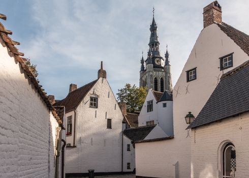 Kortrijk, Flanders, Belgium - September 17, 2018: Spire of Notre Dame church seen from Corner of beguinage with white and red roofed housing. Some green foliage.