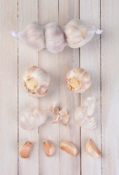 Overhead view of garlic on a rustic white table. Three bulbs in a net bag, two bulbs below the bag, scattered skin pieces and four clove segments.