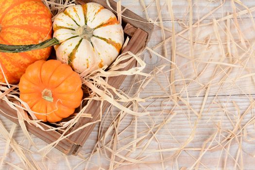 Overhead view of a wooden crate with different decorative pumpkins on a rustic wood table with straw. Horizontal format with copy space.