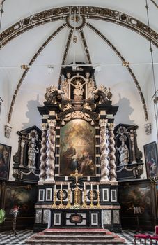 Brugge, Flanders, Belgium - September 19, 2018: Mostly black and white colors on main altar of Saint Anna Church in Bruges. Colorful painting as center and golden candles and cross. Some red carpets.