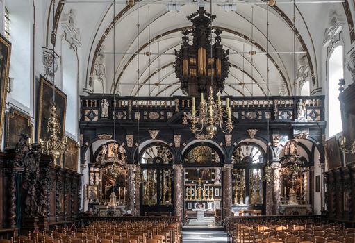 Brugge, Flanders, Belgium - September 19, 2018: Overview of separated chancel of Saint Anna Church in Bruges. Dark wood decorations and plenty of gold. Chairs up front. Altar in back.