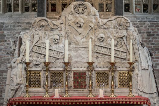 Brugge, Flanders, Belgium - September 19, 2018: Altar with red and gold decoration has a gray cement backdrop featuring skulls, bones, tools and ladders in Jerusalem Chruch of Bruges.