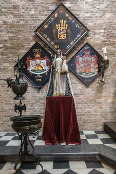 Brugge, Flanders, Belgium - September 19, 2018: Madonna statue on pedestal in Jerusalem church in Bruges. Three Family coat of arms on brick wall as backdrop.