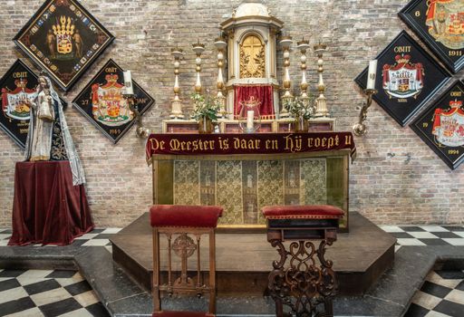 Brugge, Flanders, Belgium - September 19, 2018: Altar with tabernacle and Madonna statue on pedestal in Jerusalem church in Bruges. several Family coat of arms on brick wall as backdrop.