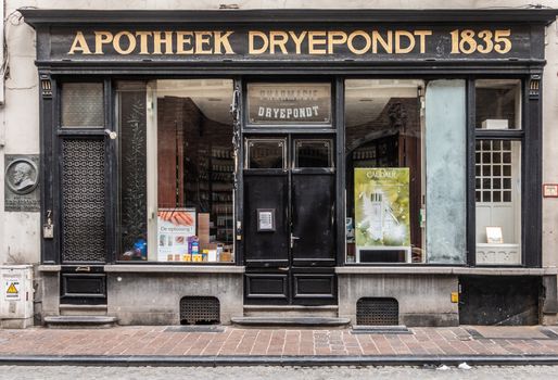 Brugge, Flanders, Belgium - September 19, 2018: Old pharmacy Dreypondt facade in Wollestraat Bruges shows display-windows in black frames. Golden characters for name. Colorful merchandise posters.