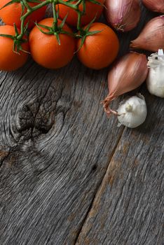 Tomatoes, onions and garlic on a rustic wood kitchen table. Vertical format with copy space.