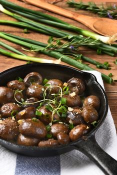 High angle vertical view of sauteed mushrooms in a cast iron skillet surrounded by ingredients and utensils.