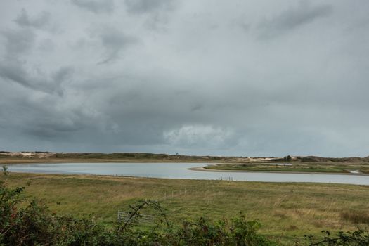 Knokke-Heist, Belgium - September 22, 2018: Wide shot of the green Zwin plane with seawater marshes under heavy rainy dark cloudscape. Horizon features Het Keun statue in center.