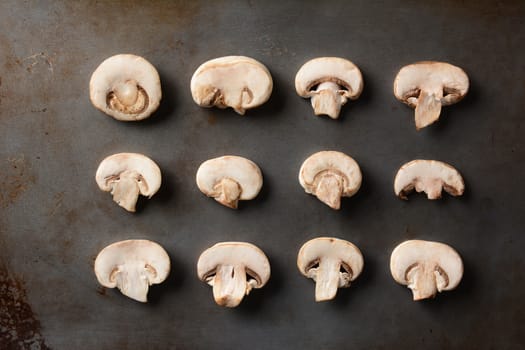 Rows of sliced mushrooms on a metal baking sheet. High angle shot in horizontal format.