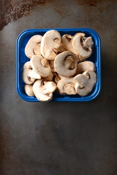 A Blue container of sliced mushrooms on a metal baking sheet. High angle shot in vertical format.