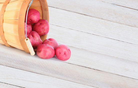 High angle shot of a basket full of red potatoes spilling onto a rustic wood table. horizontal format with copy space.