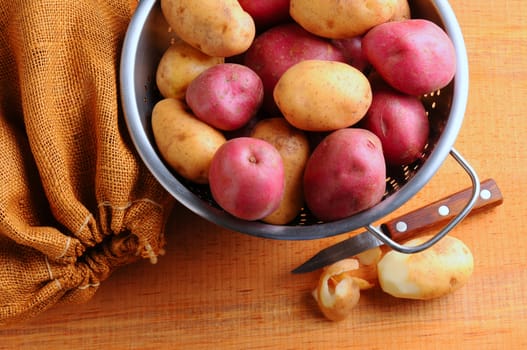 Potatoes in Colander with Burlap Sack and Paring Knife. Horizontal format shot from high angle.