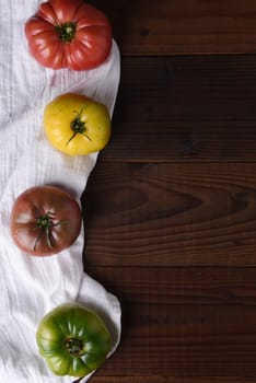 Top view of heirloom tomatoes on a kitchen towel and dark wood table.