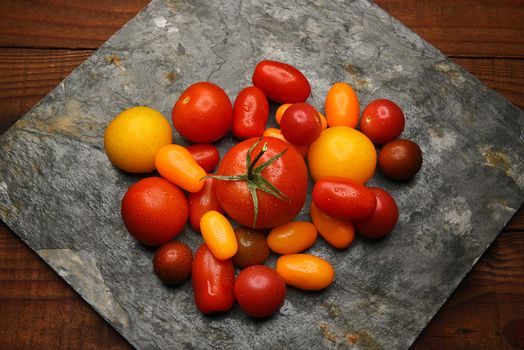 Top view of a group of Medley Tomatoes on a slab of slate on a rustic wood surface.