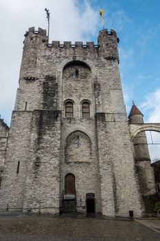 Ghent, Belgium - September 23, 2018: Central gray stone tower of the Castle of Gent. Flag of Flanders and of Ghent on top. Blue sky with white clouds.