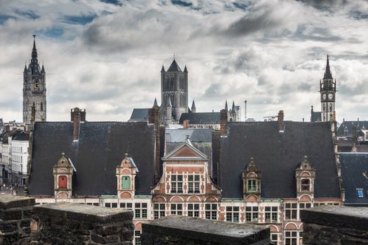 Ghent, Belgium - September 23, 2018: Seen from Gent Castle tower. Three towers LTR: Belfry, Saint Nicolas church, Postal clock tower. Under heavy cloudscape of white on blue. Facades of Sint Veerleplein.