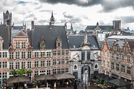 Ghent, Belgium - September 23, 2018: Seen from Gent Castle tower. Gray statue decorated gate to historic fish market among red brick facades of historic houses now restaurants. Cloudscape and towers on horizon.