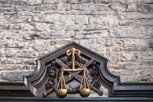 Ghent, Belgium - September 23, 2018: Balance symbol as Justice is enforced by the swords as seen in Gent Gravensteen Castle. Gray stone wall with black frame and golden symbol.