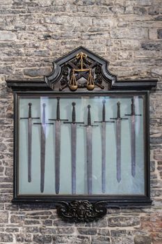 Ghent, Belgium - September 23, 2018: Balance symbol as Justice is enforced by the swords as seen in Gent Gravensteen Castle. Gray stone wall with black frame, golden symbol and collection of swords.