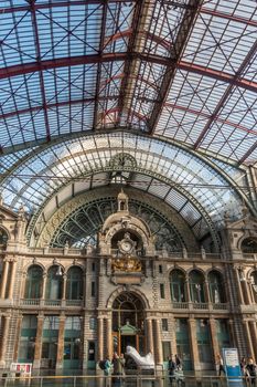Antwerp, Belgium - September 24, 2018: Portrait, Historic Train hall facade of Antwerpen Central Station, considered nicest train station in world. Glass roof, golden emblem, clock, facade and people.