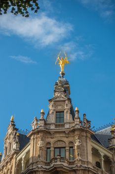 Antwerp, Belgium - September 24, 2018: Golden lightning carrying angel statue on top of brown stone facade on corner of Meir and Otto Veniusstraat against blue sky, More statues.