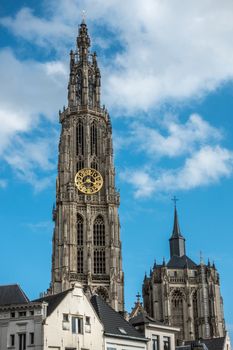 Antwerp, Belgium - September 24, 2018: Closeup of Towers of Onze-Lieve-Vrouwe Cathedral of Our Lady in back under blue cloudy sky. Parts of white facades up front.