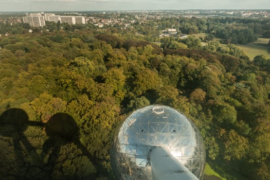 Brussels, Belgium - September 25, 2018: One shining metalic sphere and shadows of others of the Atomium monument. Shot from above with green Laken Park as background.