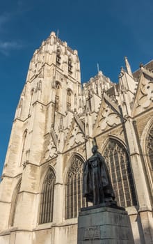 Brussels, Belgium - September 26, 2018: Yellow stone Towers of Cathedral of Saint Michael and Saint Gudula with bronze statue of Cardinal Mercier in front. Blue sky.