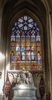 Brussels, Belgium - September 26, 2018: Stained Glass Window of Cathedral of Saint Michael and Saint Gudula. White stone tomb monument in front.