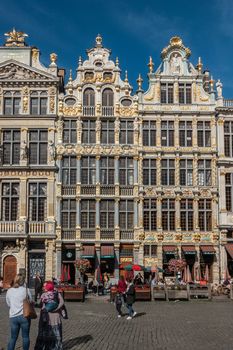 Brussels, Belgium - September 26, 2018: Three brown stone facades with golden decorations and statues on Grand Place against blue sky. People walking on square.