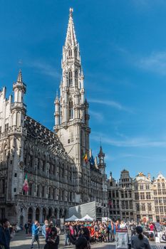 Brussels, Belgium - September 26, 2018: Town hall with its gray stone spire on the Grand Place, Grote Markt, with plenty of people and facades of other houses with golden statues. Blue sky.