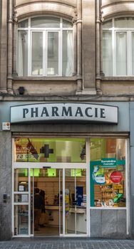 Brussels, Belgium - September 26, 2018: Mosest pharmacie store front in Rue Des Fripiers downtown advertises cosmetics. People in store. Second level windows in beige facade.