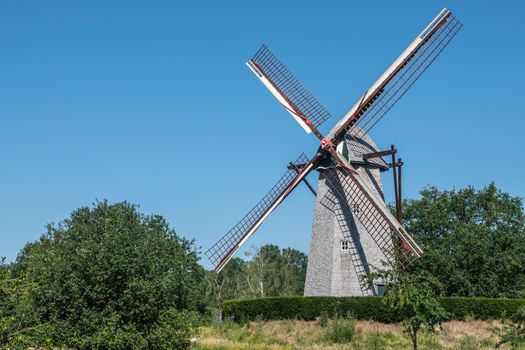 Bokrijk, Belgium - June 27, 2019: Windmill of Schulen is set in green environment of meadow and surrounded by trees under blue sky. No sails on wings.