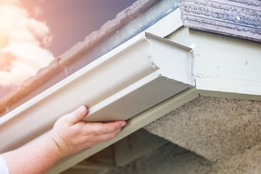 Worker Attaching Aluminum Rain Gutter to Fascia of House.