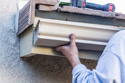 Worker Attaching Aluminum Rain Gutter to Fascia of House.