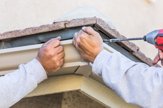 Workers Attaching Aluminum Rain Gutter to Fascia of House.