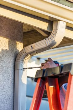 Worker Attaching Aluminum Rain Gutter and Down Spout to Fascia of House.