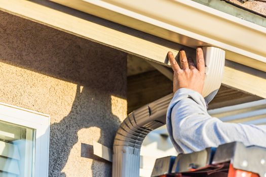 Worker Attaching Aluminum Rain Gutter and Down Spout to Fascia of House.