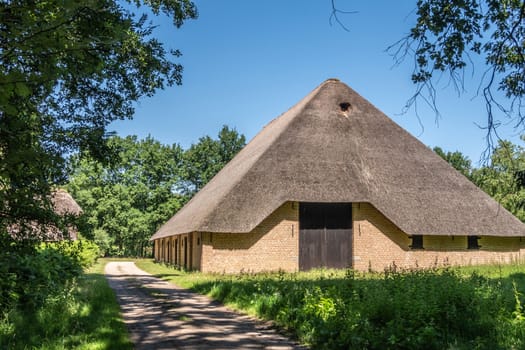 Bokrijk, Belgium - June 27, 2019: Giant barn with gray straw roof is set in green of meadow and surrounding trees under blue sky.