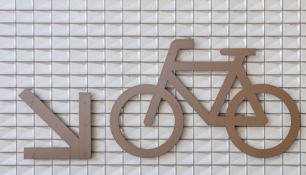 Amsterdam, the Netherlands - June 30, 2019: Closeup of giant bike parking sign with direction marker down on white wall at IJdok.