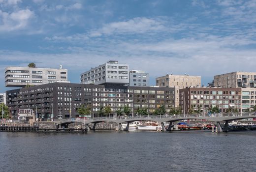 Amsterdam, the Netherlands - June 30, 2019: Modern architecture office buildings on Westerdoksdijk has sections with dark walls and other parts on top with white gray walls. Blue sky. Pedestrian bridge to IJdok.
