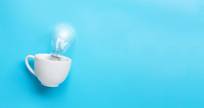 Light bulb in white cup on blue background. Ideas and creative thinking concept. Copy space