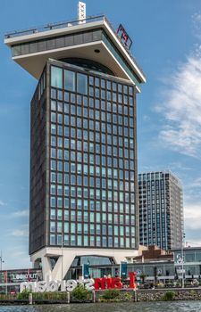 Amsterdam, the Netherlands - June 30, 2019: A’Dam lookout tower under blue sky with some white clouds. IJ water in front. Iconic Amsterdam sign. Daredevil swing in red on top.